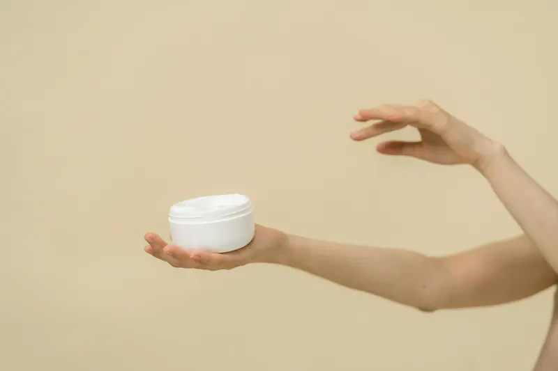 Unas manos sostienen un tarro abierto de crema para la piel