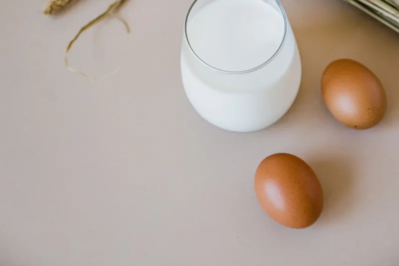 Un vaso de leche, huevos y espigas sobre una mesa