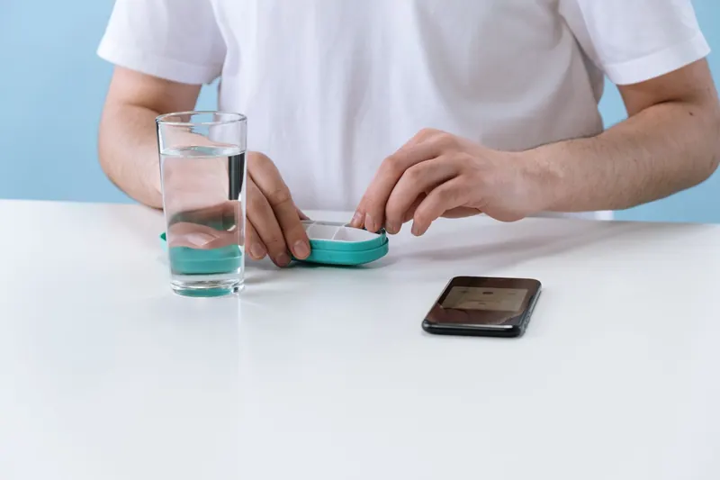 Una persona organiza medicación junto a un vaso de agua